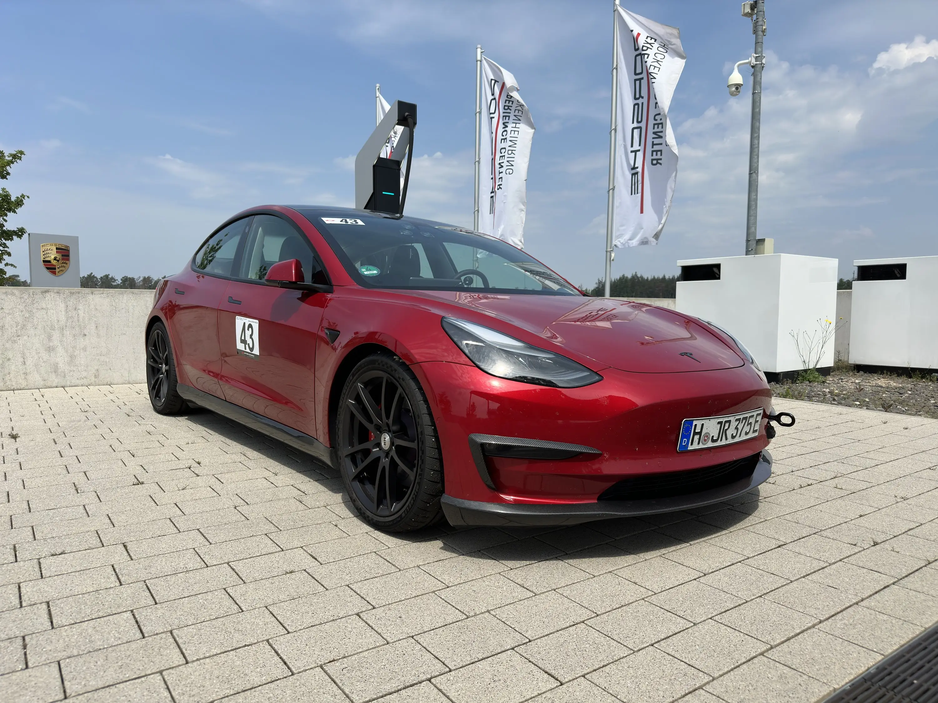 Rotes Tesla Model 3 Performance „Red Devil“ mit Startnummer 43 an der Tür und schwarzen Felgen, Schrägansicht von vorn vor dem Porsche Experience Center, Hockenheimring, 22. Mai 2023.