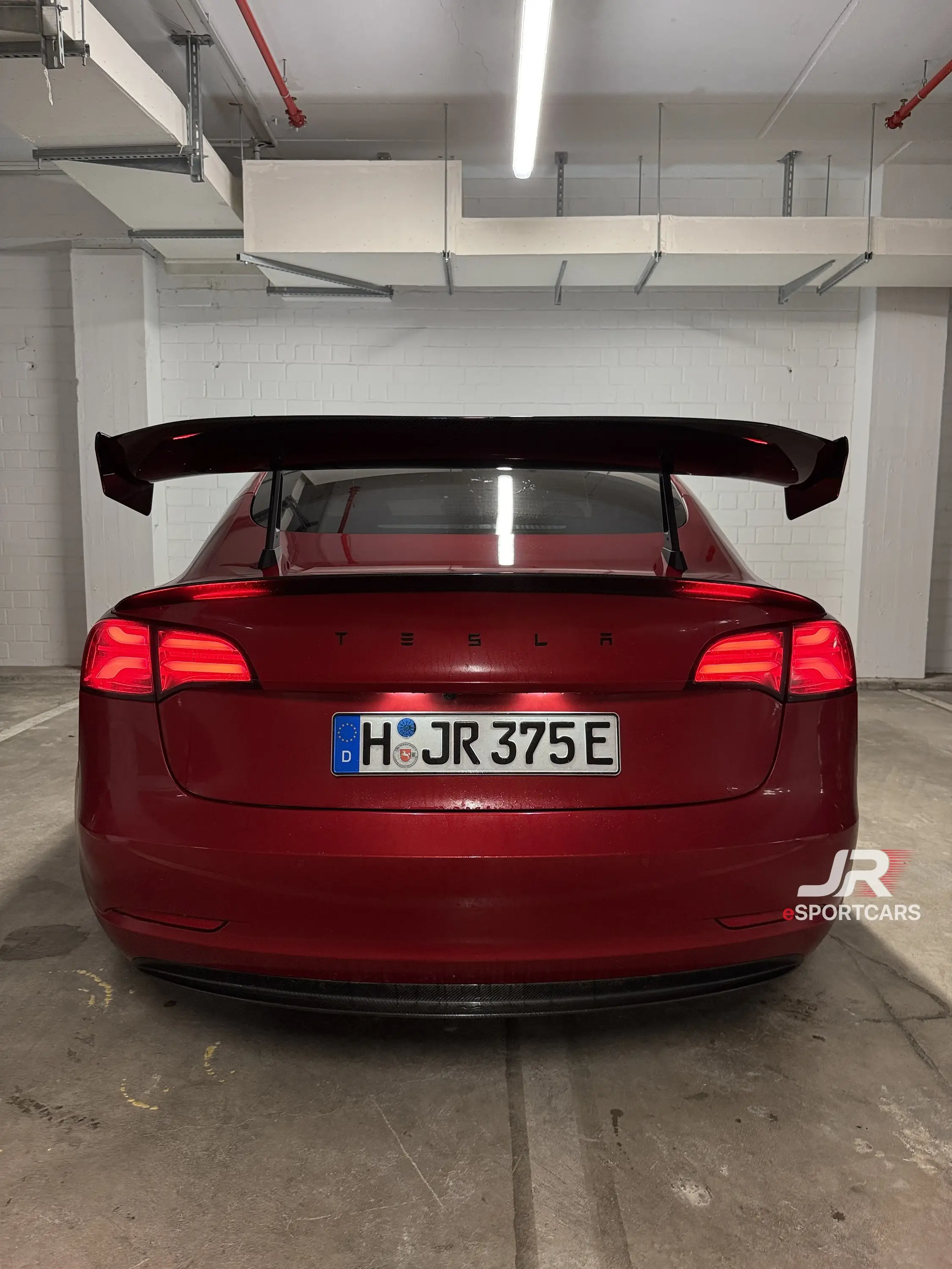 Rotes Tesla Model 3 mit großem Heckflügel, Heckansicht in einer Tiefgarage.