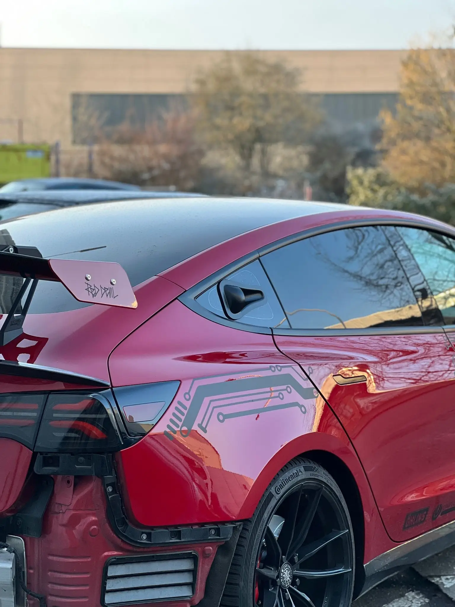 Rotes Tesla Model 3, Heck von schräg hinten ohne Heckstoßstange, Flügel-Endplatte mit „Red Devil“-Schriftzug.