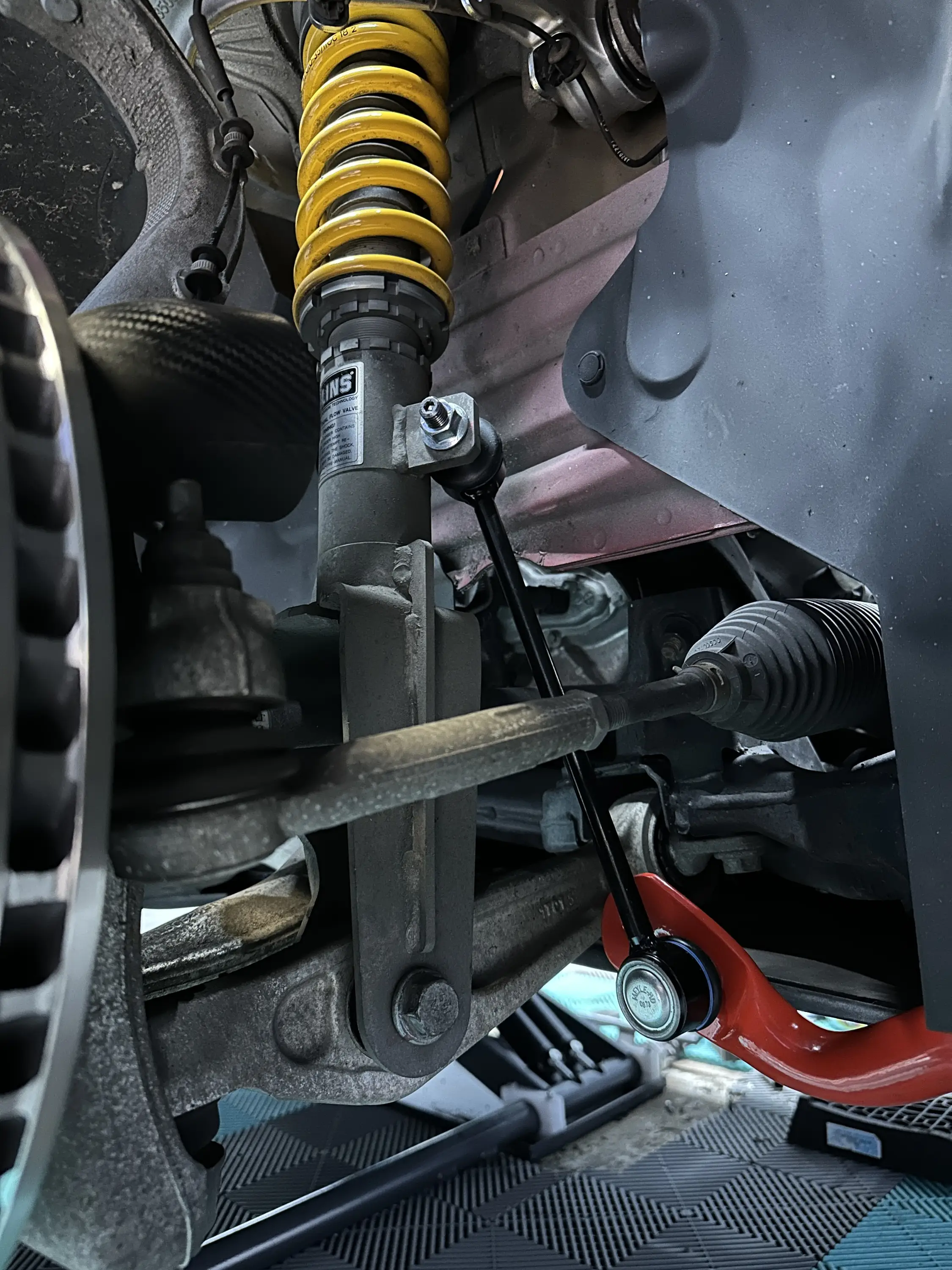 Vorderachse von unten: Öhlins-Federbein mit gelber Feder, Spurstange, rote Fahrwerksteile und Bremsscheibe.