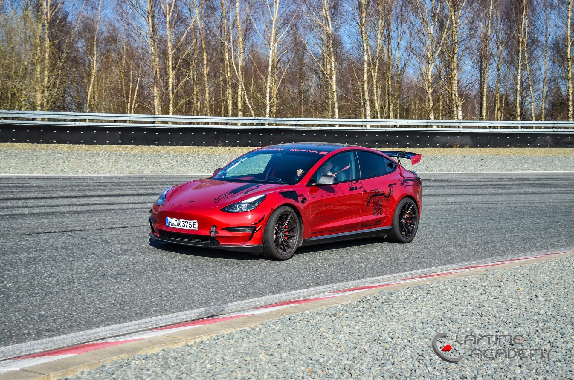 Rotes Tesla Model 3 Performance „Red Devil“ auf der Rennstrecke, Schrägansicht von vorn, Wasserzeichen „Laptime Academy“.